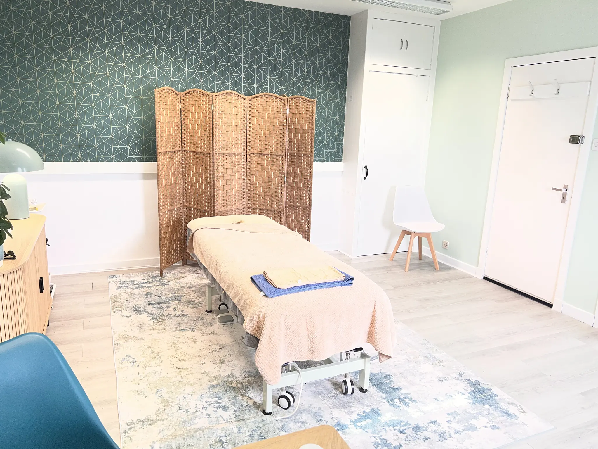 The adjustable massage bed laid with towels in front of a woven screen and green geometric wallpaper