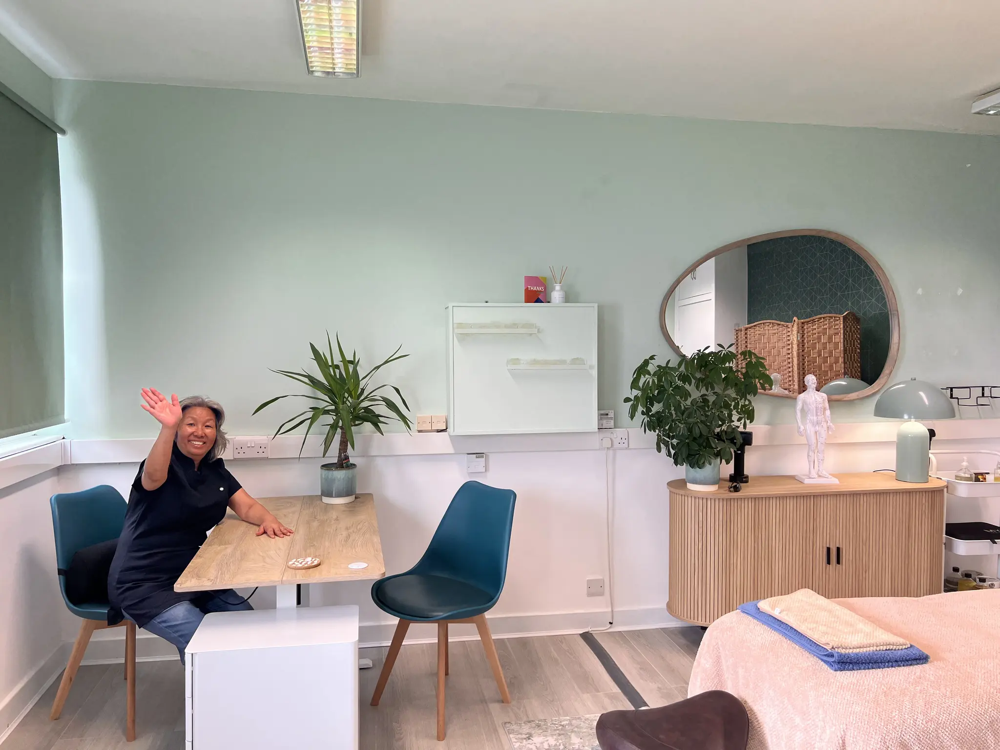 Shi Shi waving from the consultation table at the far side of the bright treatment room