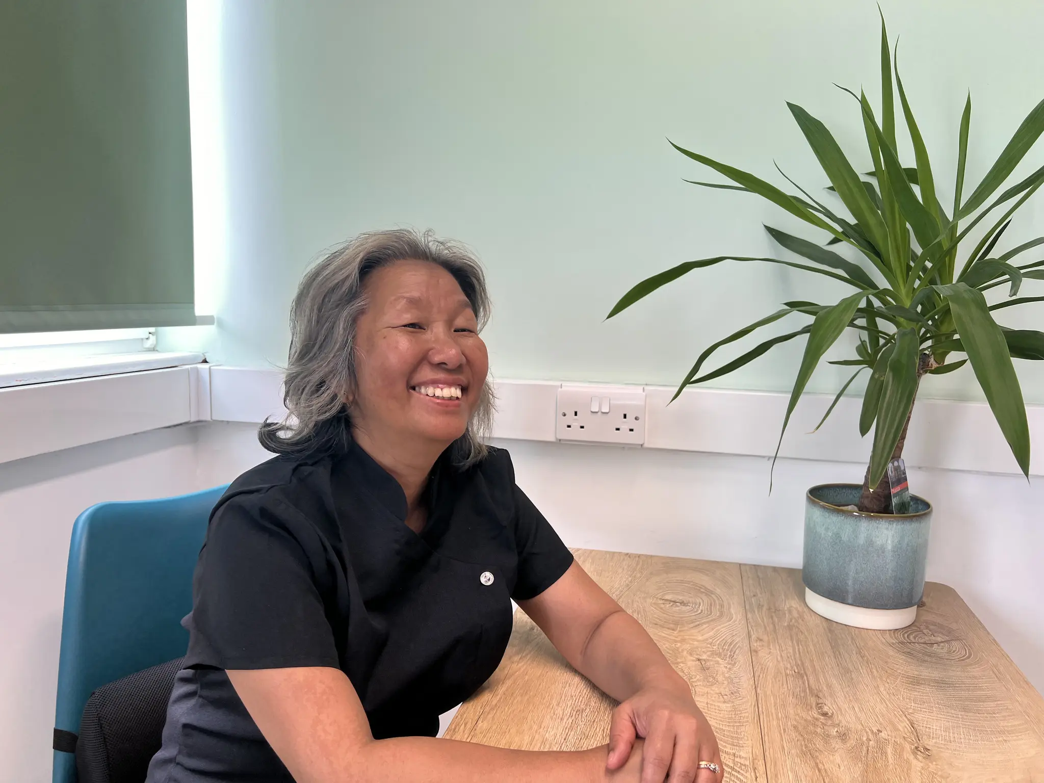 Shi Shi smiling at the consultation desk beside a tall potted plant